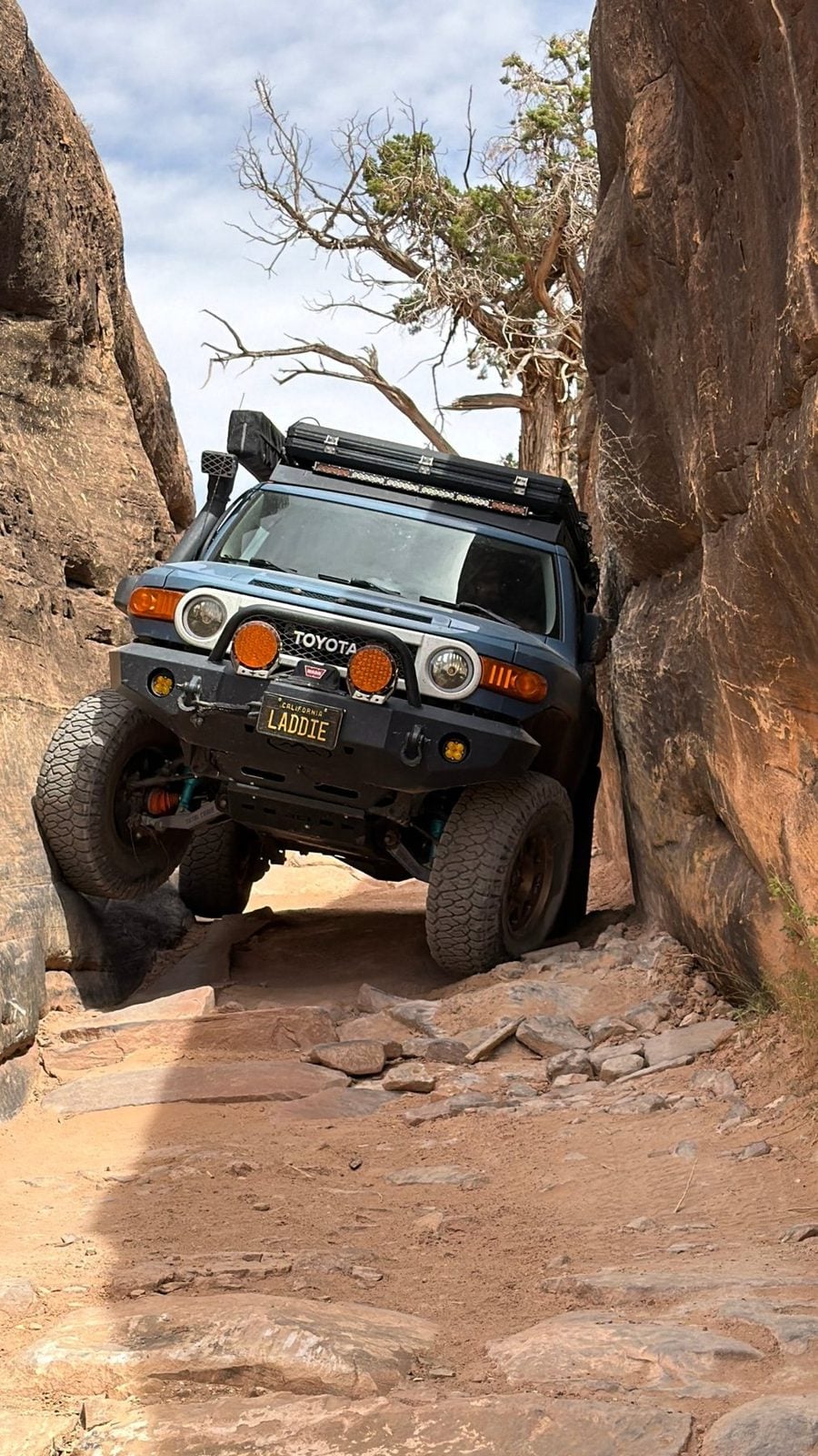 Blue FJ Cruiser flexed through a sandstone slot, one front wheel in the air